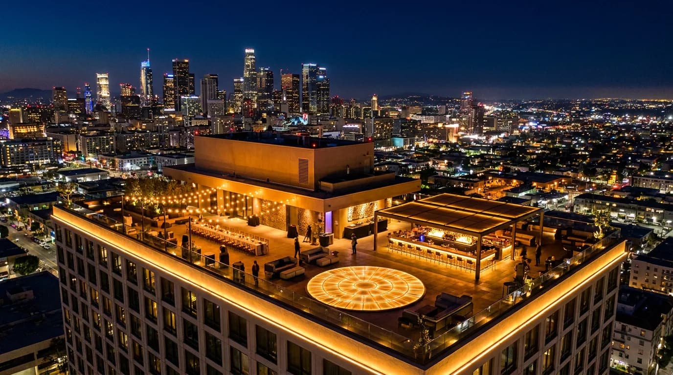 Rooftop event at night overlooking the downtown Los Angeles skyline, with string lights, lounge seating, a bar, and catering tables set for a celebration